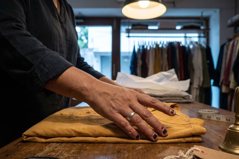A shopkeeper smoothing a folded mustard garment on a worn wooden counter