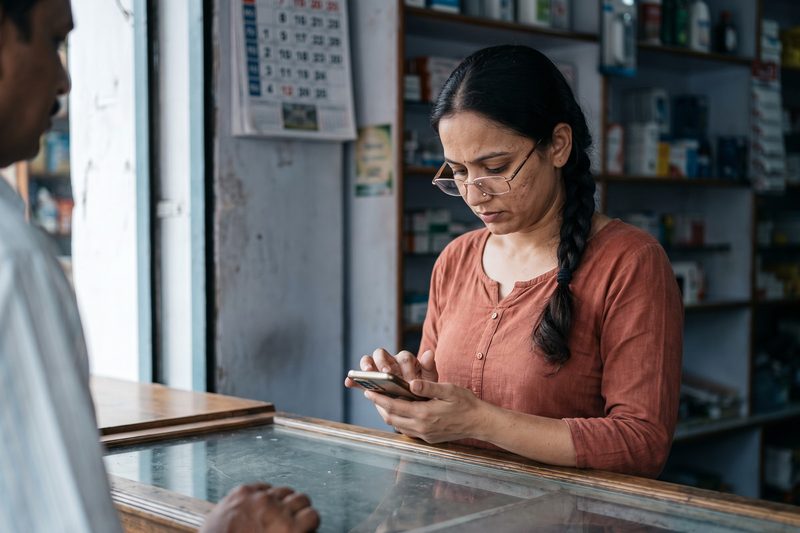 A young woman behind a shop counter replying to a customer on her phone