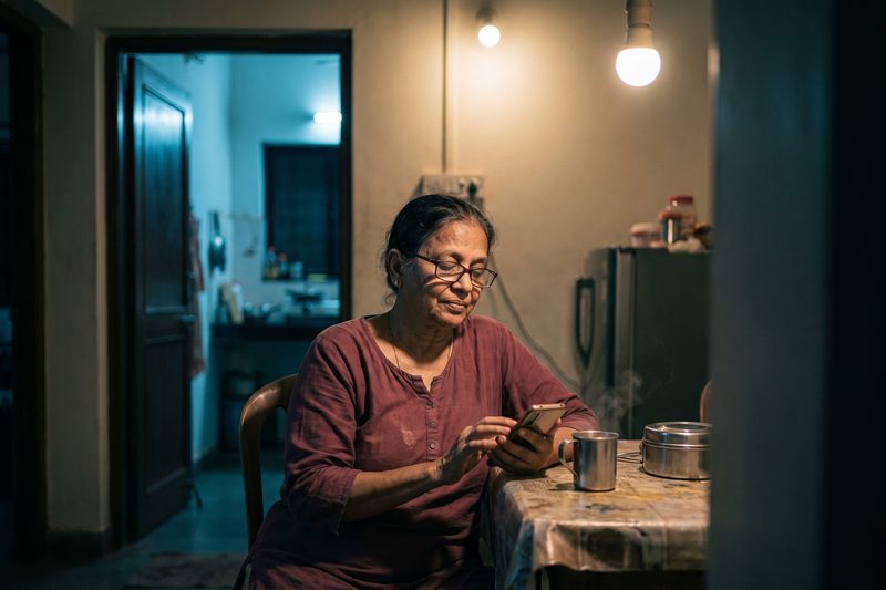 A shop owner at home in the evening with a cup of chai, reading the day's report on her phone