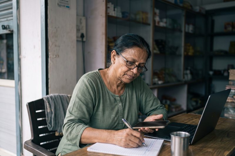 A shop owner at her counter writing down a step while someone walks her through setup on a call